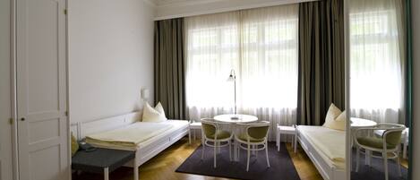 A hotel room with two single beds, a round table with chairs, a small desk, and a mirror.