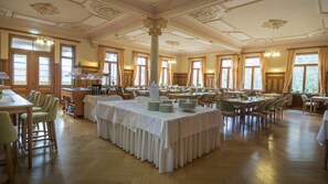 A spacious banquet hall with multiple tables set for dining, a central column, and large windows allowing natural light. - Wildbad Rothenburg o.d.T. (Rothenburg ob der Tauber)