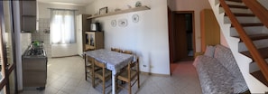 A compact kitchen with a dining area, a sofa, and a staircase.