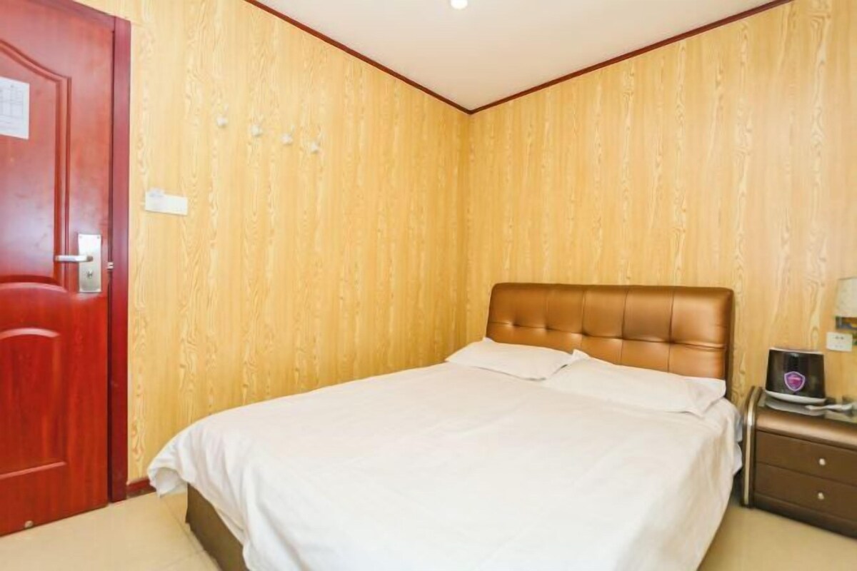 A single bed with a headboard, a wooden door, and a nightstand with a lamp.