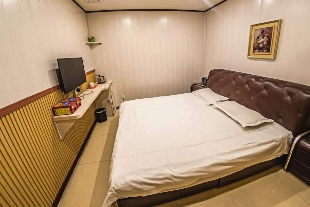 Een slaapkamer met een bed, een televisie, een klein tafeltje met een afstandsbediening en een foto aan de muur.
