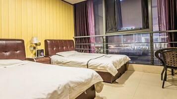 A hotel room with two beds, a window with curtains, a nightstand with a lamp, and a chair.