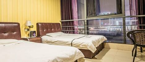 A hotel room with two beds, a window with curtains, a nightstand with a lamp, and a chair.