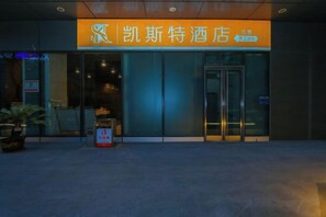 A hotel entrance with a prominent sign, a reception desk, and a glass door.