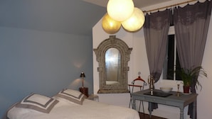Un dormitorio con cama, escritorio, silla, lámpara, espejo y ventana con cortinas.