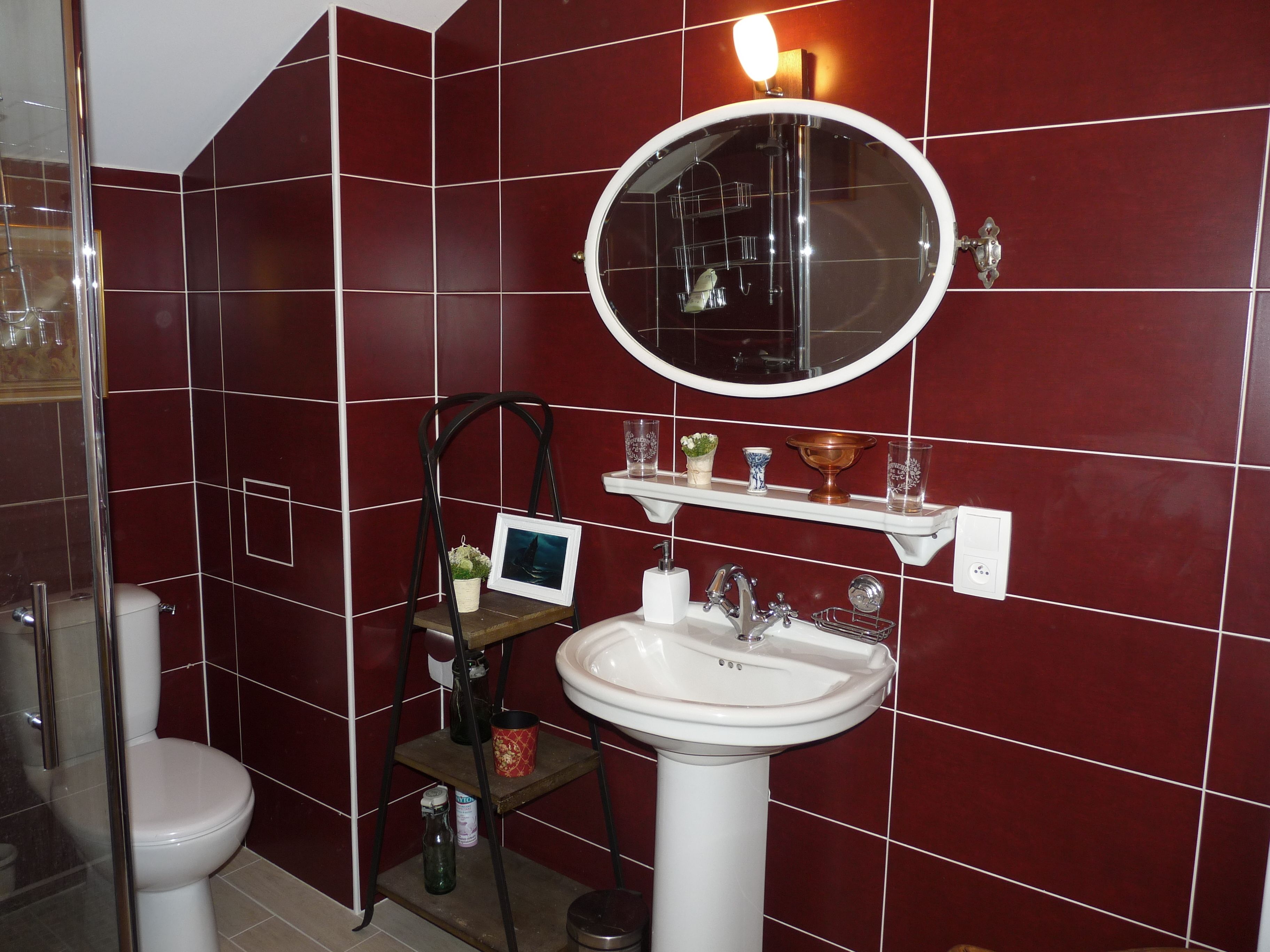 A bathroom with a white sink, a round mirror, and a shelf with toiletries.