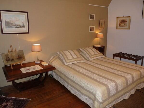 Ein ordentlich eingerichtetes Schlafzimmer mit einem Bett, Nachttischen, einem Schreibtisch mit Lampe und gerahmten Bildern an den Wänden.