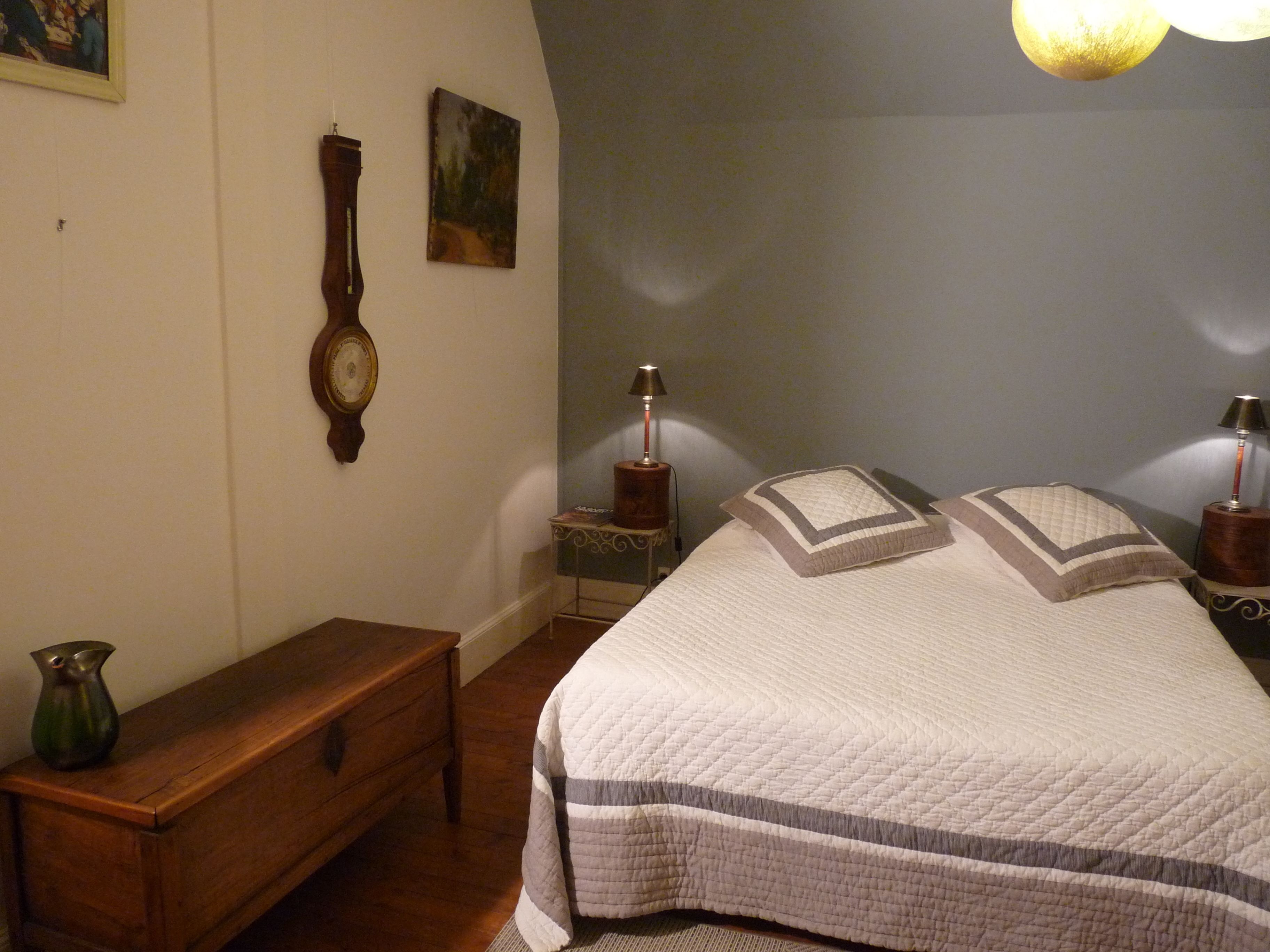 A bedroom with a large bed, a wooden bench, a wall clock, a painting, and two bedside lamps.