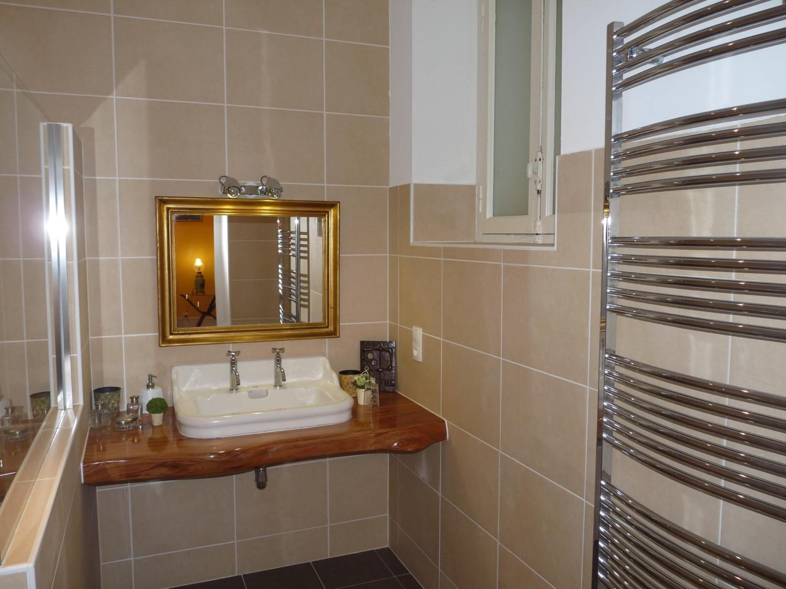 A bathroom with a wooden vanity, a white sink, a gold-framed mirror, and a towel rack.