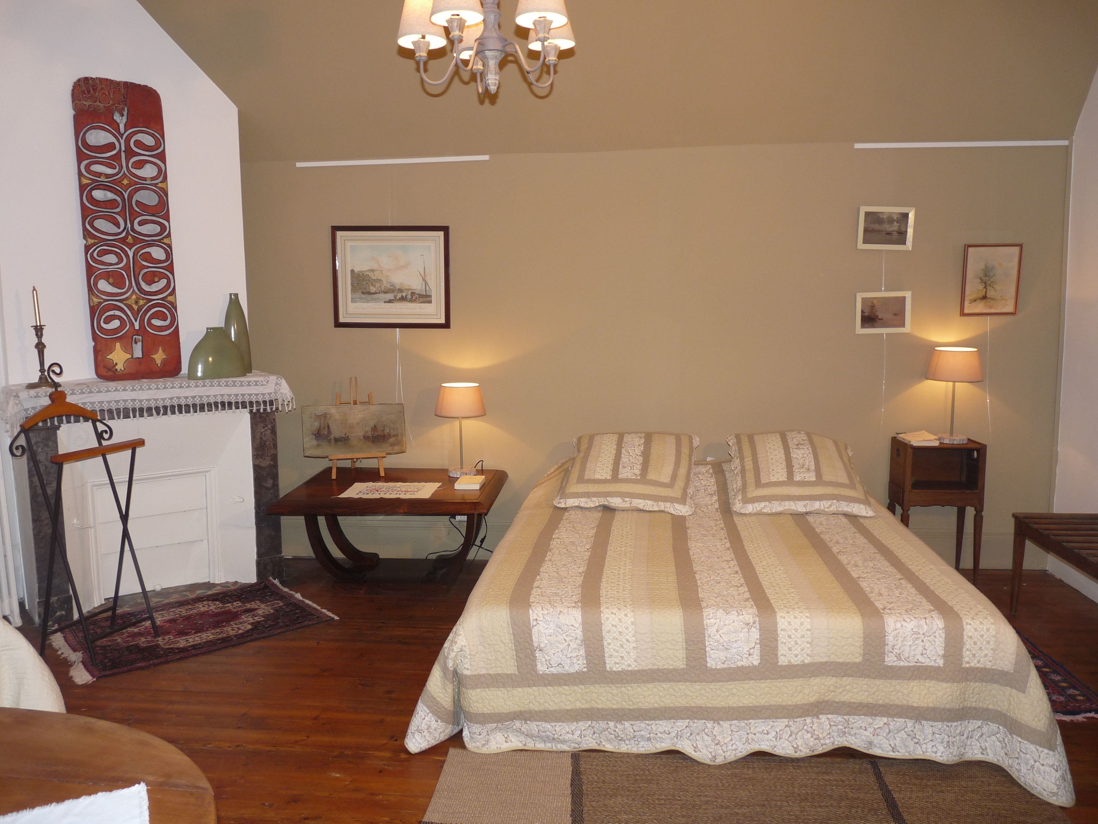 A bedroom with a bed, two bedside tables, a lamp, a painting, and a decorative wall hanging.