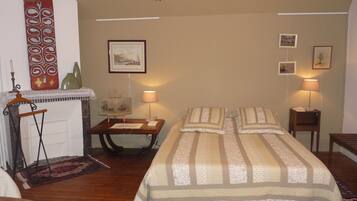 A bedroom with a bed, two bedside tables, a lamp, a painting, and a decorative wall hanging.