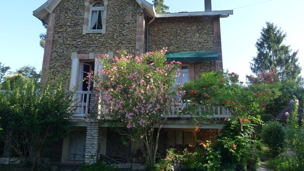 Una casa de piedra con techo a dos aguas, chimenea y balcón con toldo verde.