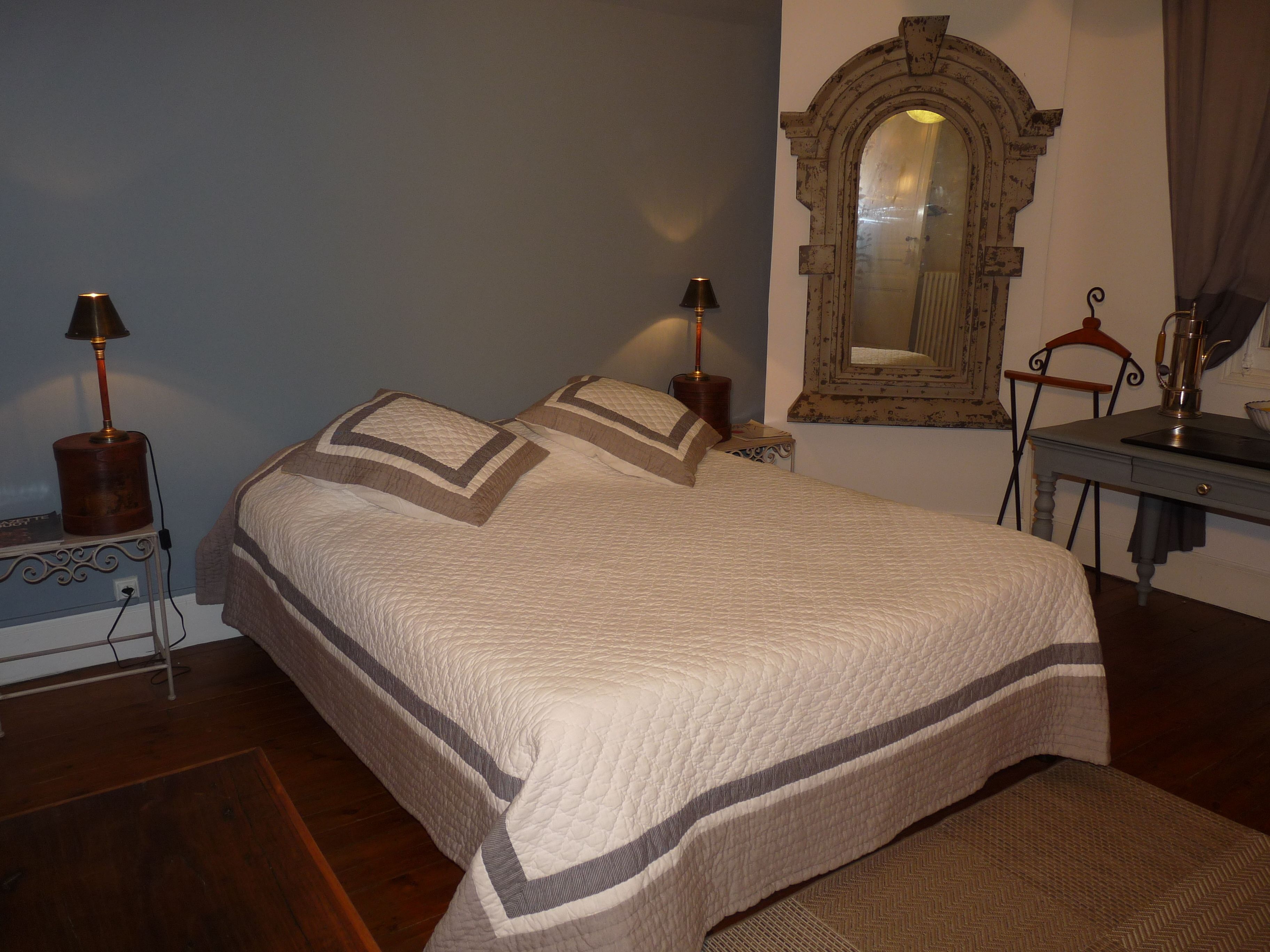 A bedroom with a large bed, two bedside lamps, a dresser, and a mirror on the wall.