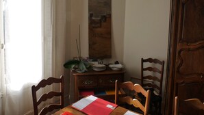 Un comedor con sillas de madera, una mesa con documentos, un armario y una ventana con cortinas.