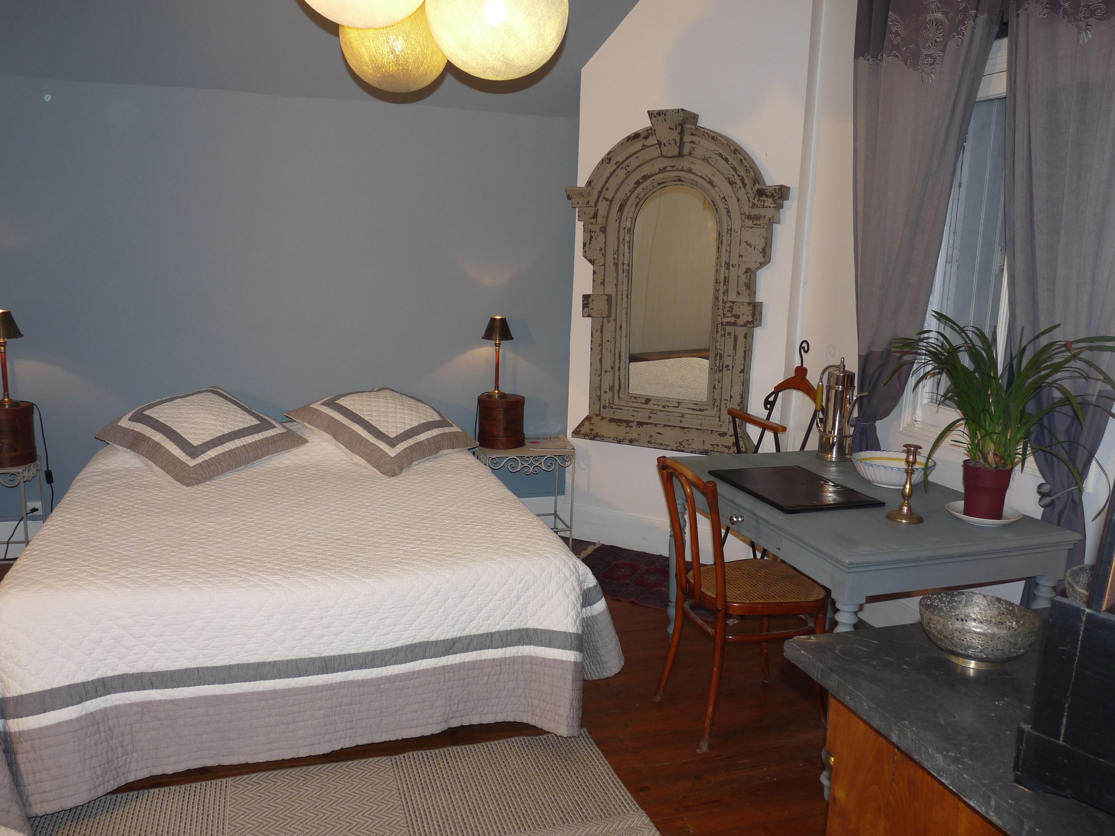 A bedroom with a bed, a desk, a chair, a mirror, and a lamp.
