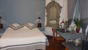 A bedroom with a bed, a desk, a chair, a mirror, and a lamp.