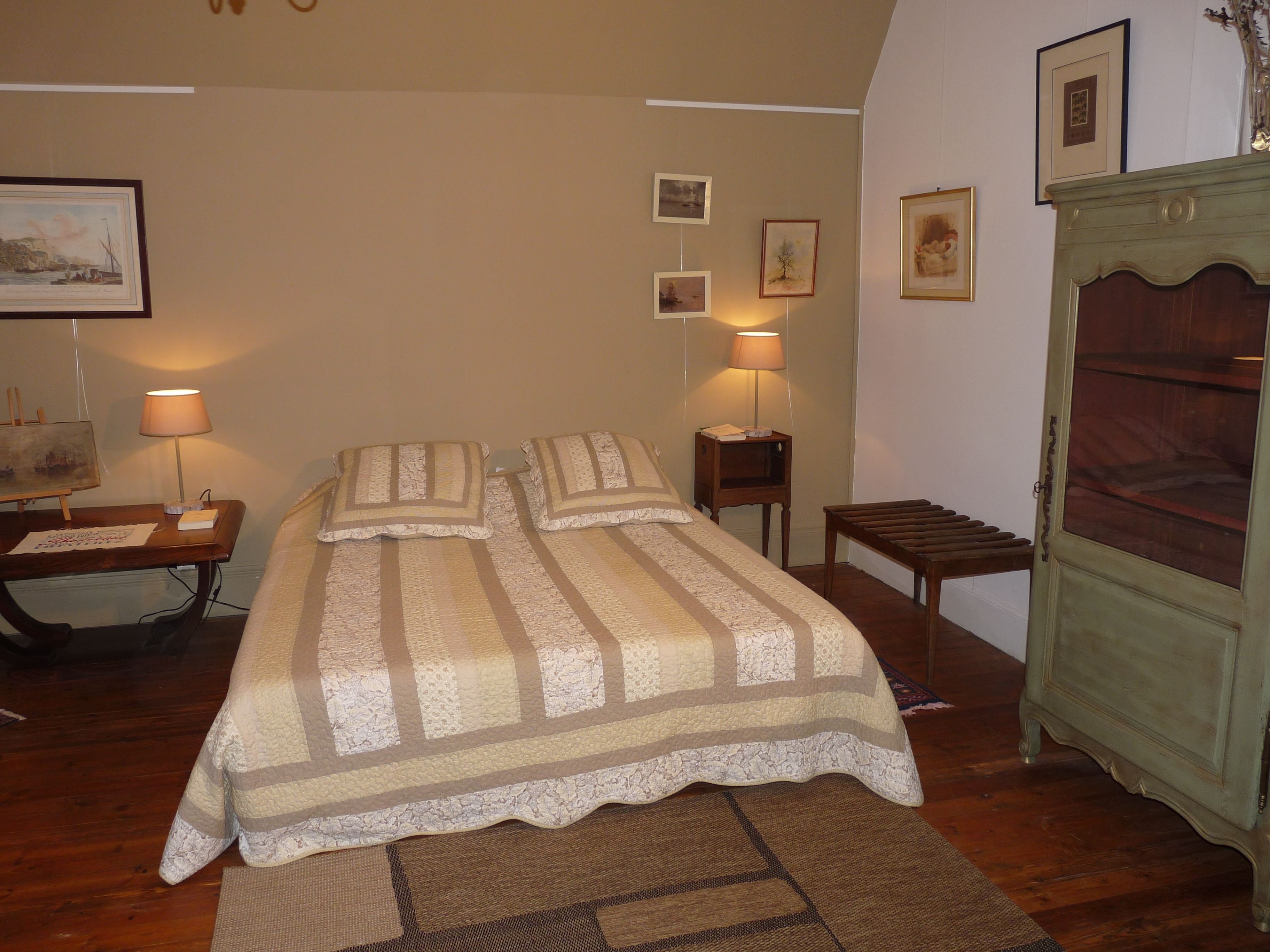 Un dormitorio con cama, lámparas de noche, mesita de noche, cómoda y cuadros en la pared.