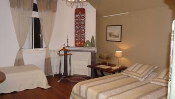 A bedroom with two beds, a dresser, a nightstand, a window with curtains, a chandelier, a painting, and a lamp.