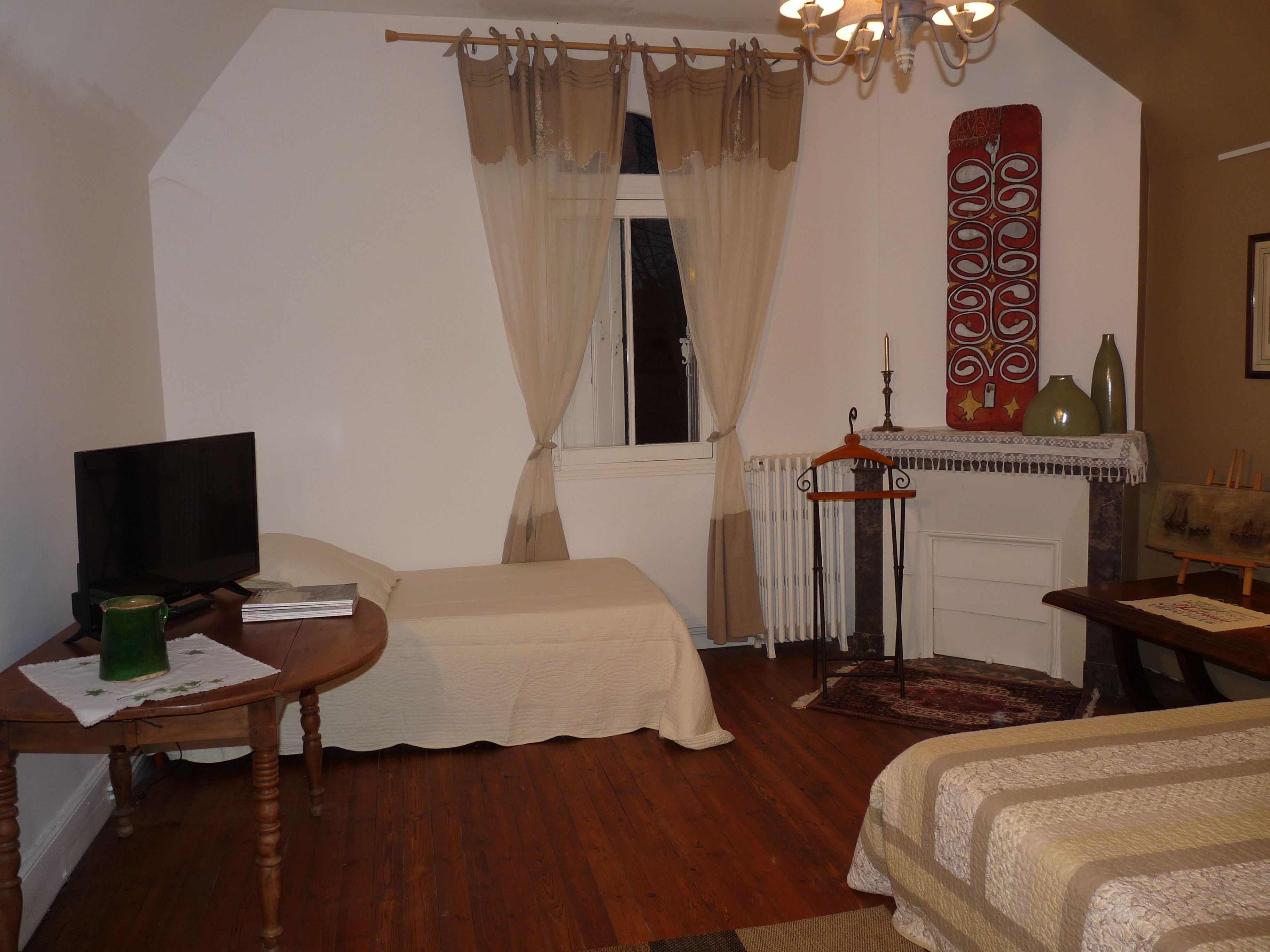 Une chambre avec un lit, une télévision, une table sur laquelle se trouve une tasse verte et une cheminée agrémentée d’objets décoratifs.