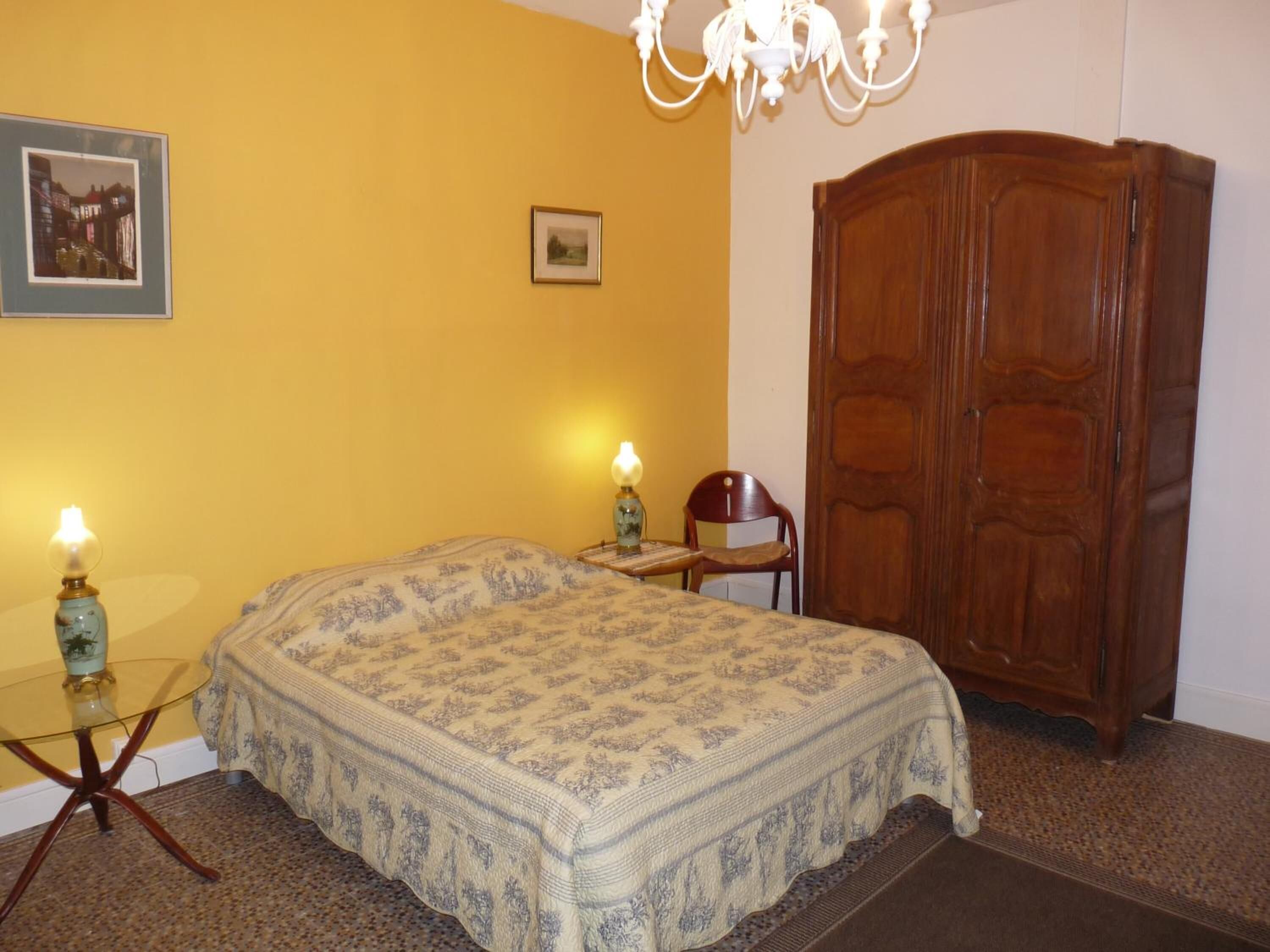 Une chambre avec un lit, deux lampes de chevet, une armoire en bois et un lustre.