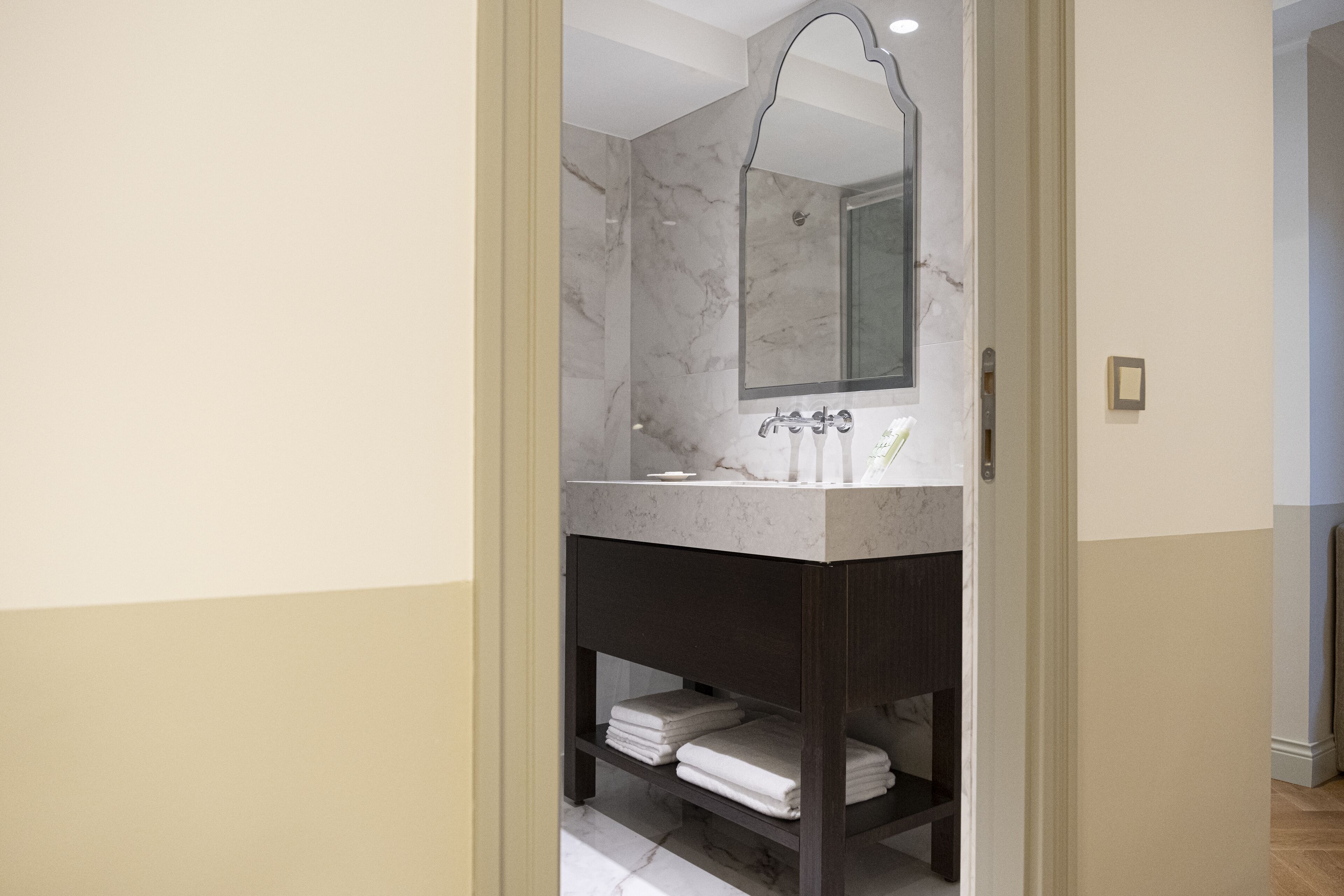 Une salle de bain moderne avec un meuble-lavabo en marbre, un grand miroir et des serviettes soigneusement pliées sur une étagère.