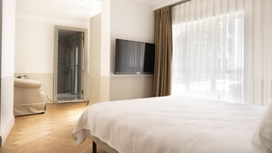 Une chambre d’hôtel avec un grand lit, un téléviseur fixé au mur, un canapé et un espace douche.