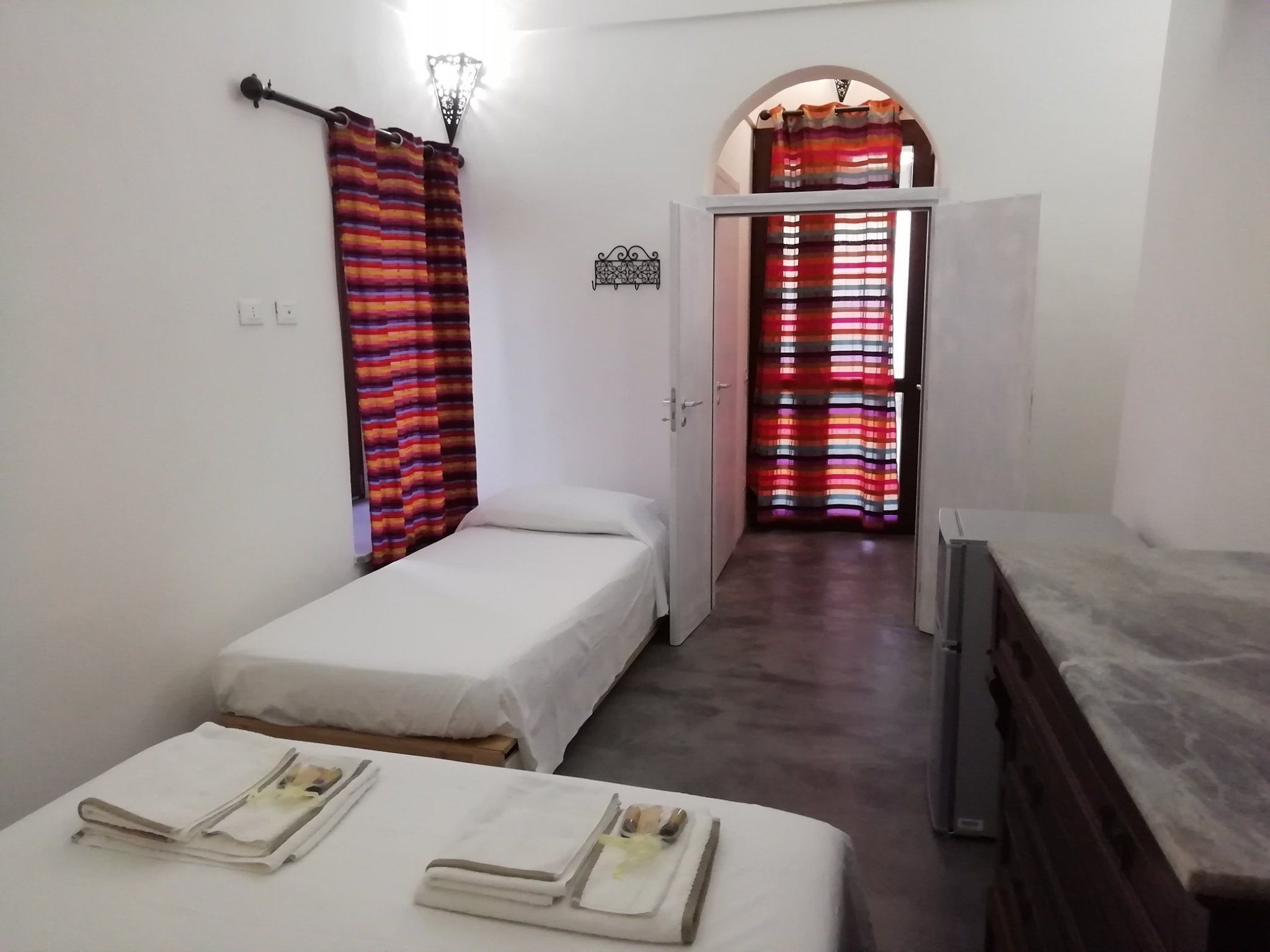 Une petite chambre propre, avec deux lits simples, un bureau et une salle de bain équipée d’un rideau de douche.