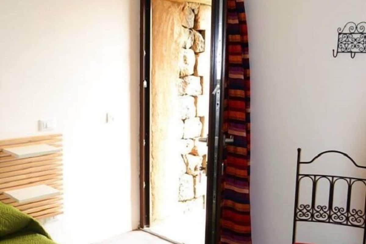 Une pièce avec un lit, une chaise rouge, une étagère en bois et une porte avec un rideau.