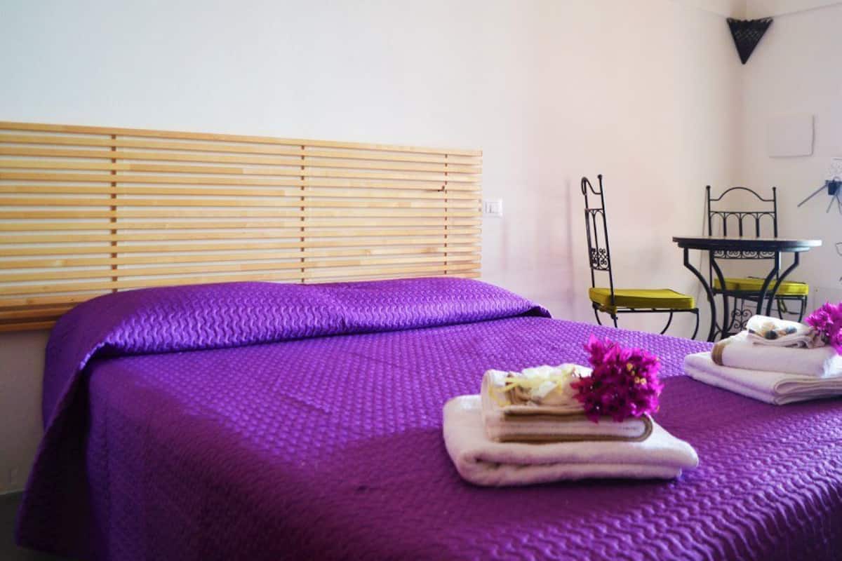 Une chambre avec deux lits, des stores en bois, une petite table et une chaise.