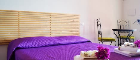 Una habitación con dos camas, persianas de madera, una mesita y una silla.