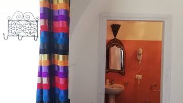 A bathroom with a tiled floor, a sink, a mirror, and a toilet. There is a colorful curtain hanging in the doorway.