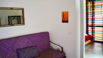 A room with a purple patterned sofa, a small framed artwork, and a colorful striped curtain.