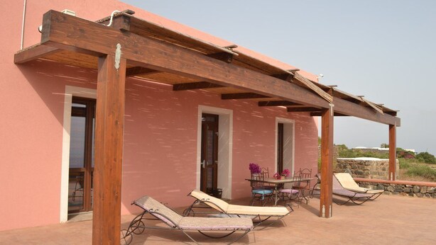 Een overdekt buitengebied met houten pergola balken, een tafel met stoelen, en twee lounge stoelen.