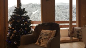 Una habitación acogedora con un árbol de Navidad, un sillón de madera y vistas a un bosque nevado a través de amplios ventanales.