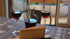 Una mesa con queso, dos copas de vino tinto, una botella de líquido oscuro y un cuchillo sobre un mantel estampado.