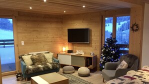 Una sala de estar acogedora con interior de madera, un televisor de pantalla plana en la pared, un árbol de Navidad y un sofá con una manta de piel.