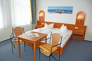 Hotelkamer met een bed, twee stoelen, een tafel, een lamp, een foto aan de muur en een raam met gordijnen.