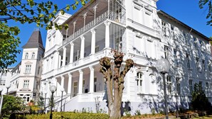 A white building with a balcony, columns, and a tower. - Budget room with shower/WC on corridor 22 - Wilhelms Hostel in Ostseebad Sellin (Sellin)