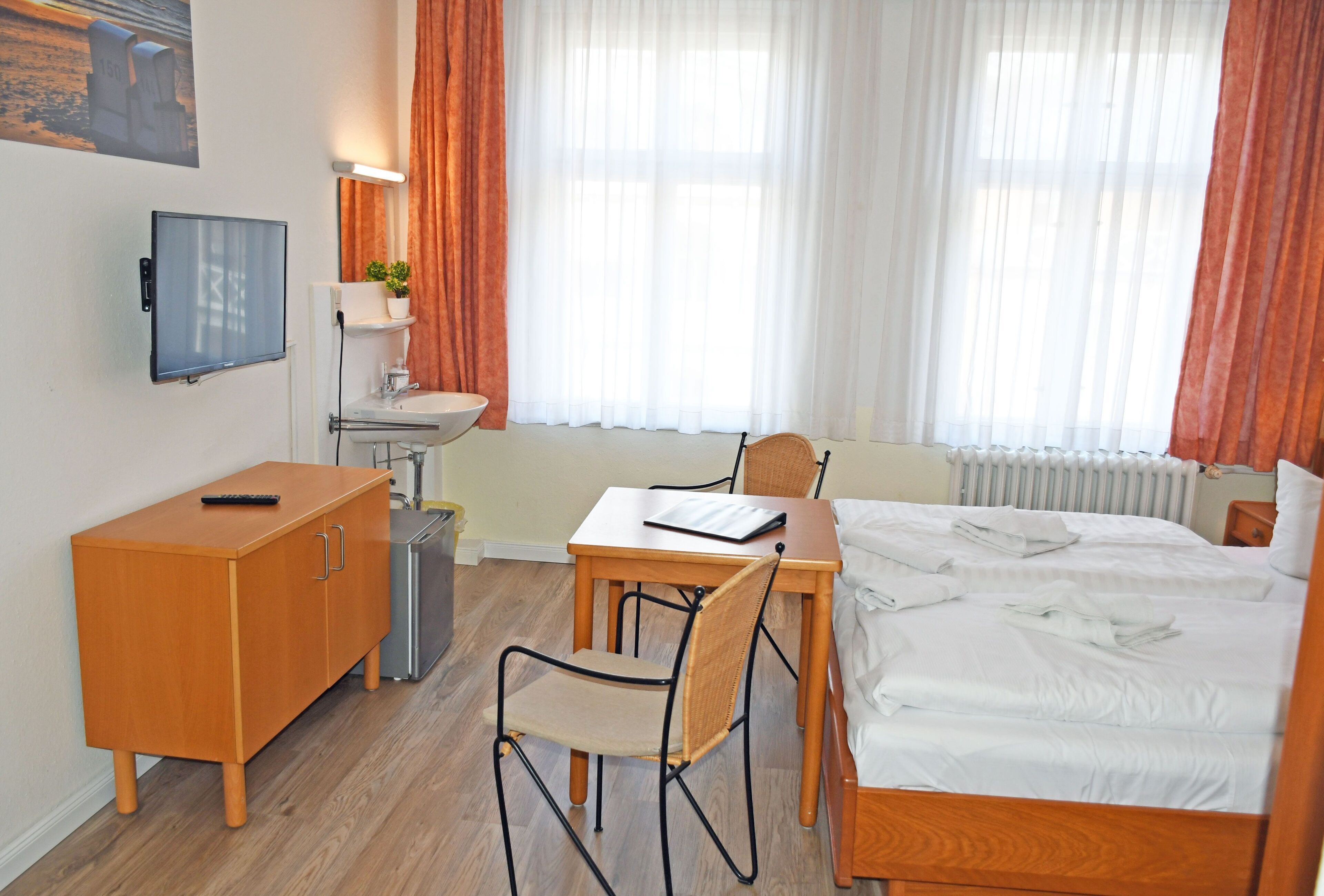Une chambre d’hôtel comprenant un lit, un bureau avec une chaise, un téléviseur fixé au mur, un lavabo et une plante en pot.