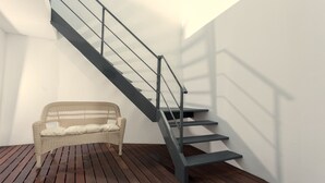 A staircase with a metal railing leading to a higher floor, a wicker sofa with cushions, and a wooden floor. - Beach House by Azores Villas (Ponta Delgada)