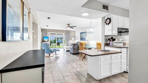 A modern kitchen with white cabinets, a granite countertop, and a dining area with a table and chairs. - Beach Service Included! Private Beach Access, Chateau La Mer 4B! (Destin)