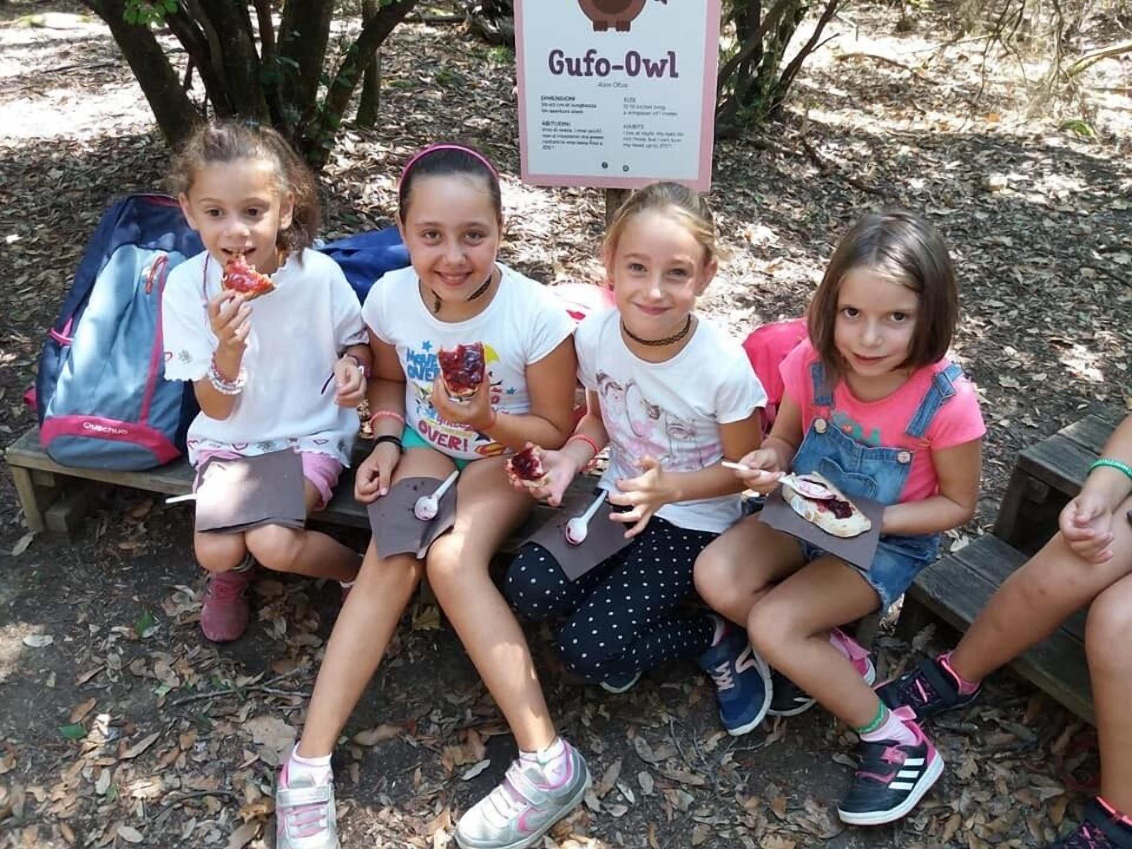 Four children sitting on a bench outdoors with a sign in the background.