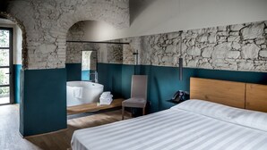 A modern bedroom with a large bed, a wooden headboard, a built-in bathtub, and a stone wall. - Palagina la cascina (Figline e Incisa Valdarno)