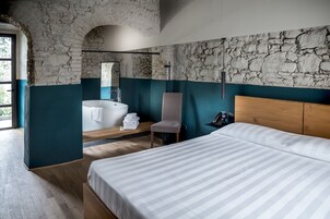 Un dormitorio moderno con una cama grande, cabecera de madera, bañera integrada y pared de piedra.