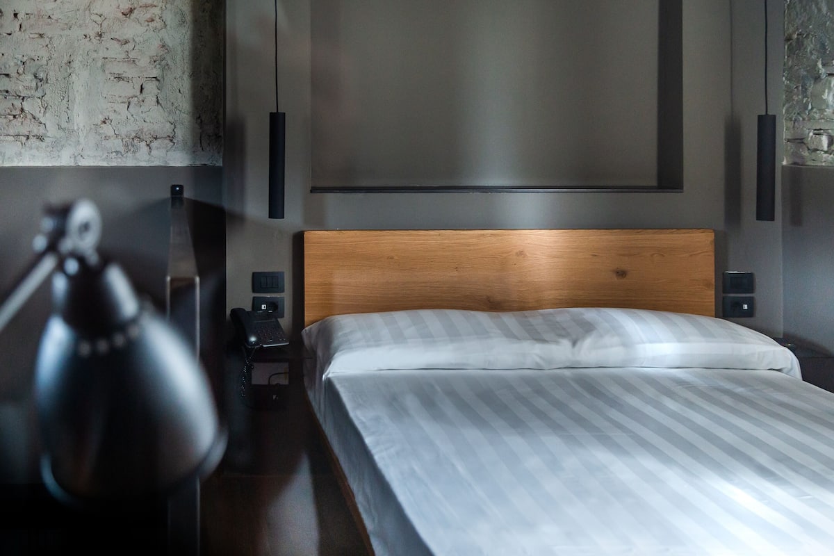 Ein modernes Schlafzimmer mit Holz-Kopfteil, einem Bett mit gestreifter Bettwäsche, einem Schreibtisch mit Lampe und einem Telefon.
