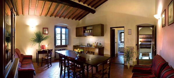 Un comedor acogedor con una mesa y sillas de madera, una cocina con armarios de madera y una sala de estar con un sofá y una planta.