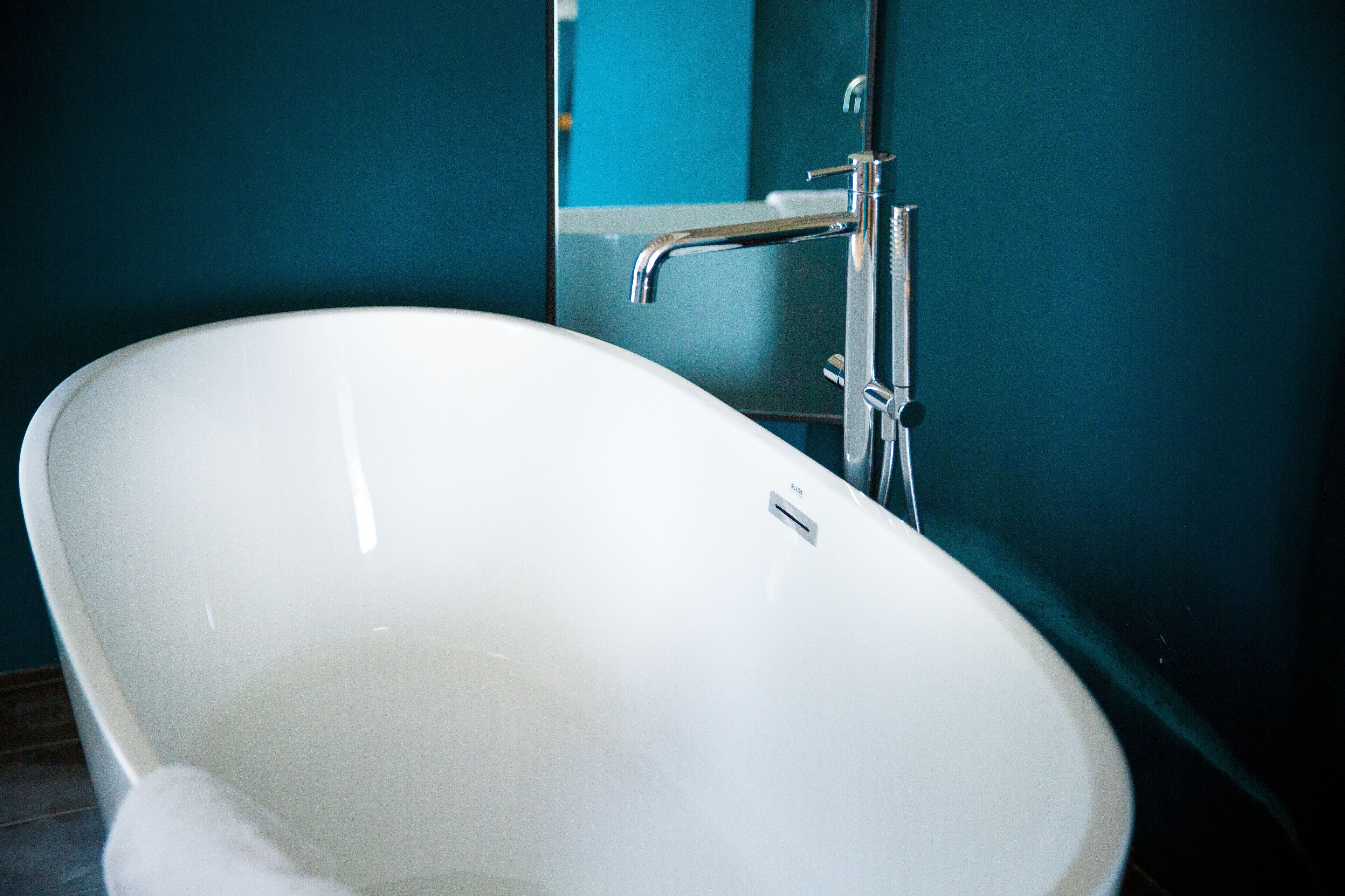Una bañera blanca independiente en un baño con paredes color turquesa.