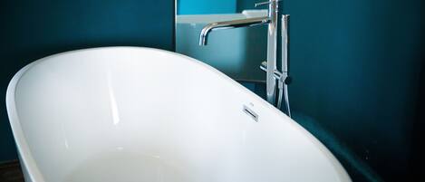 Una bañera blanca independiente en un baño con paredes color turquesa.