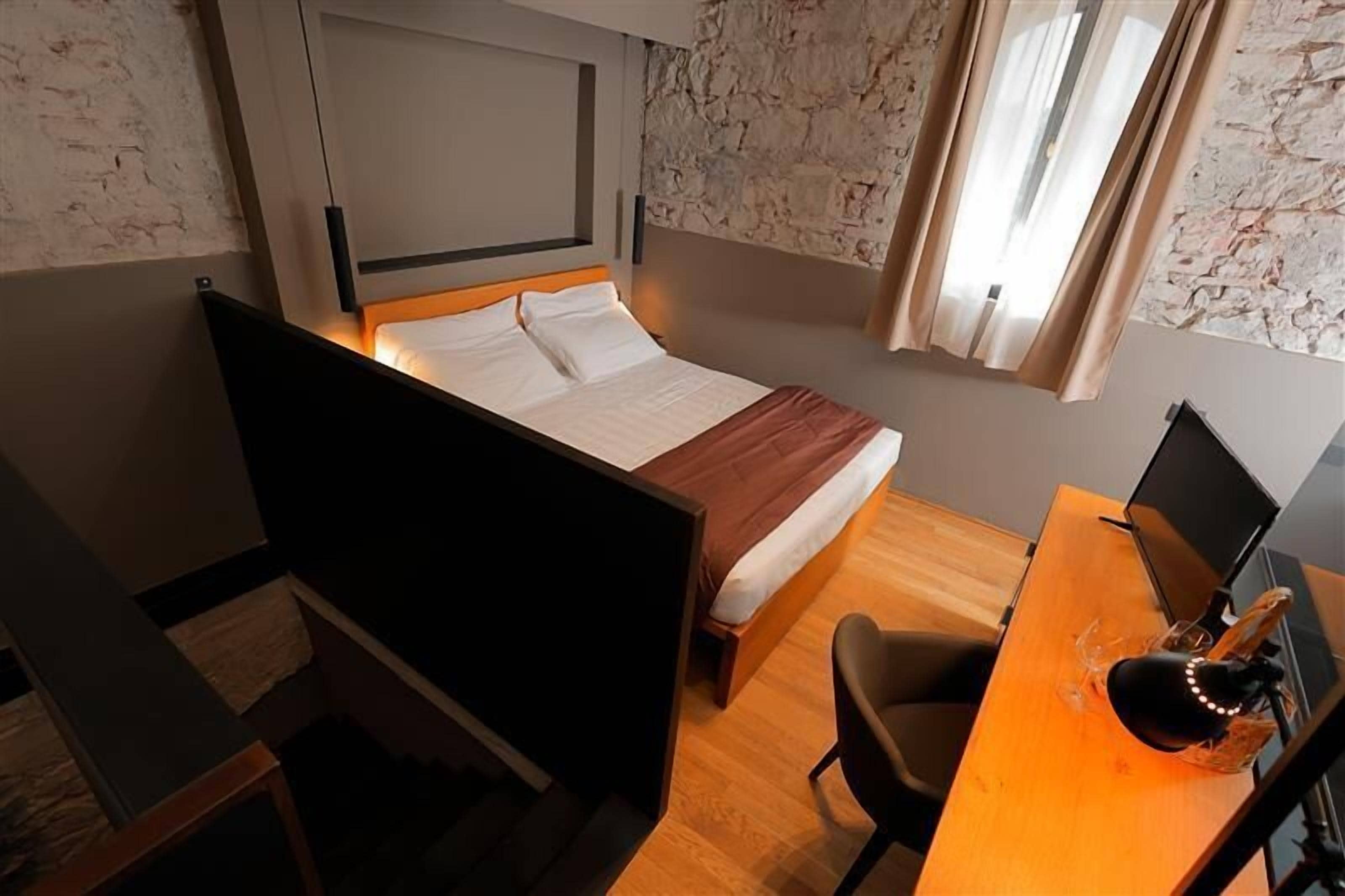A hotel room with a bed, a desk, a chair, and a TV.