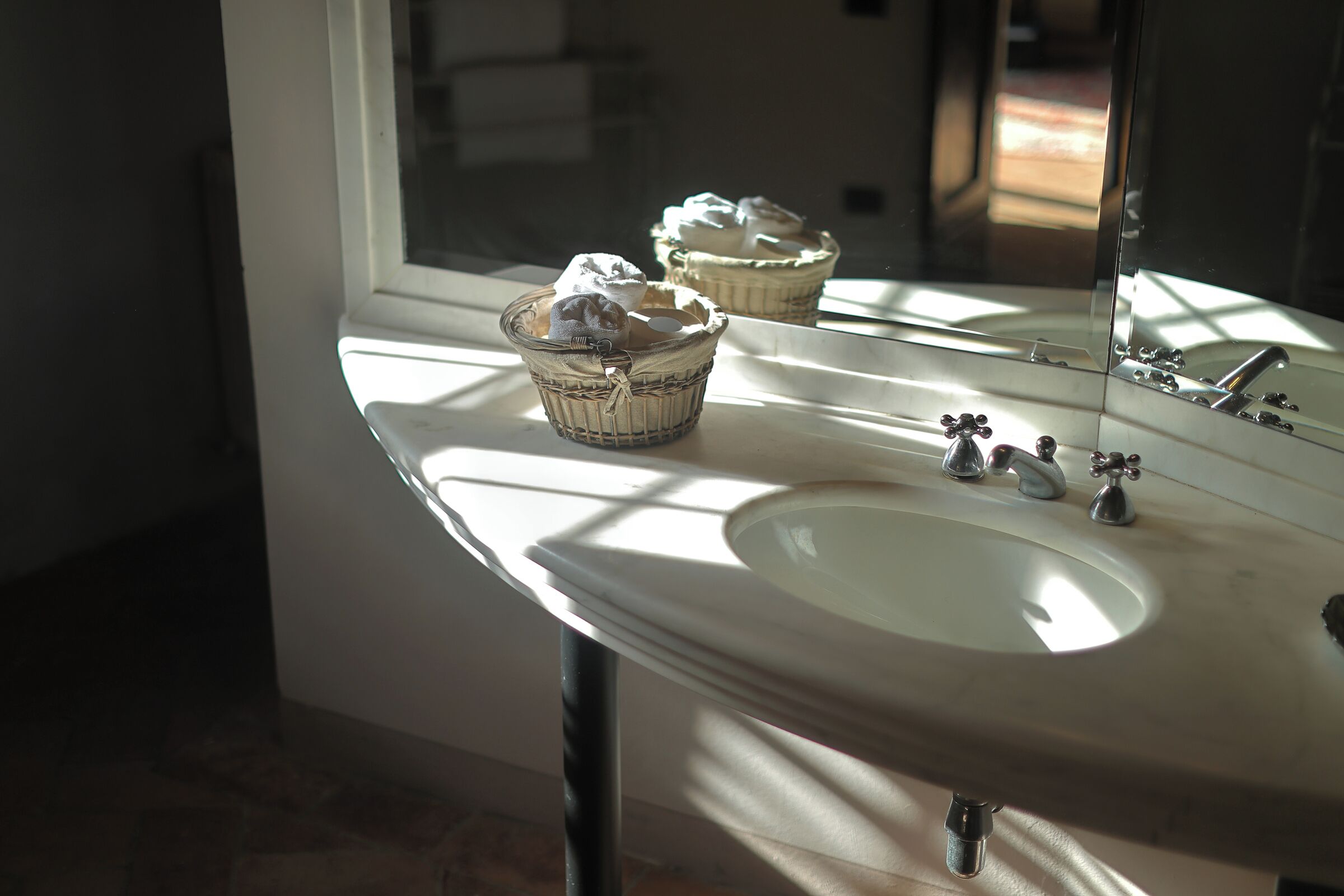 A bathroom with a white sink, two baskets with towels, and a mirror reflecting the room.